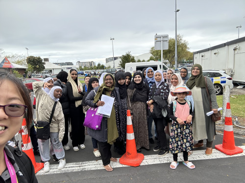 A group of women and children stand on a street behind orange road cones, smiling for the camera