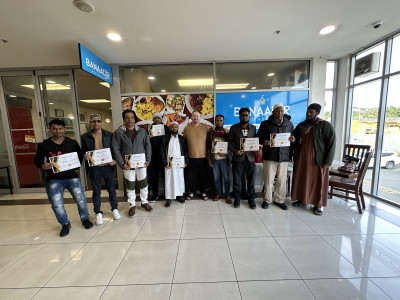 A group of men stand outside a restaurant holding certificates
